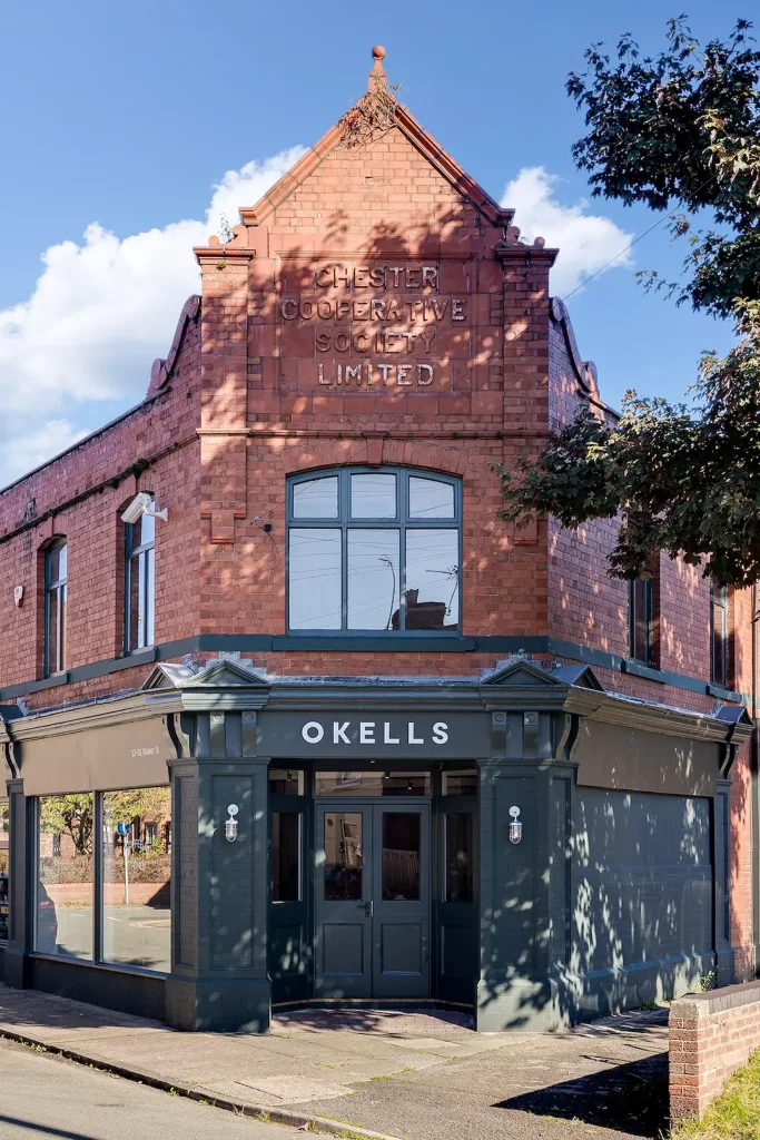 Shop front for Okells in a historic red-brick building.