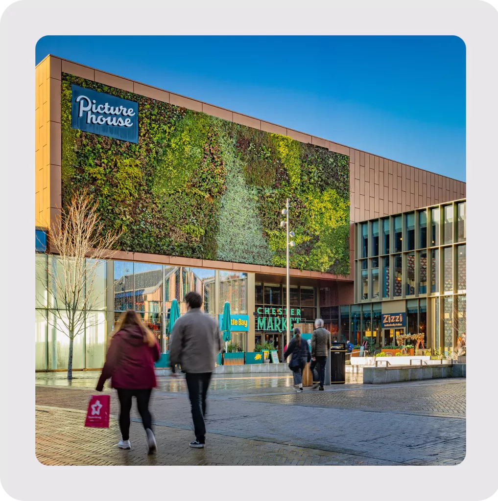 Contemporary building with a large vertical green wall and Picturehouse sign, shoppers pass Chester Market.
