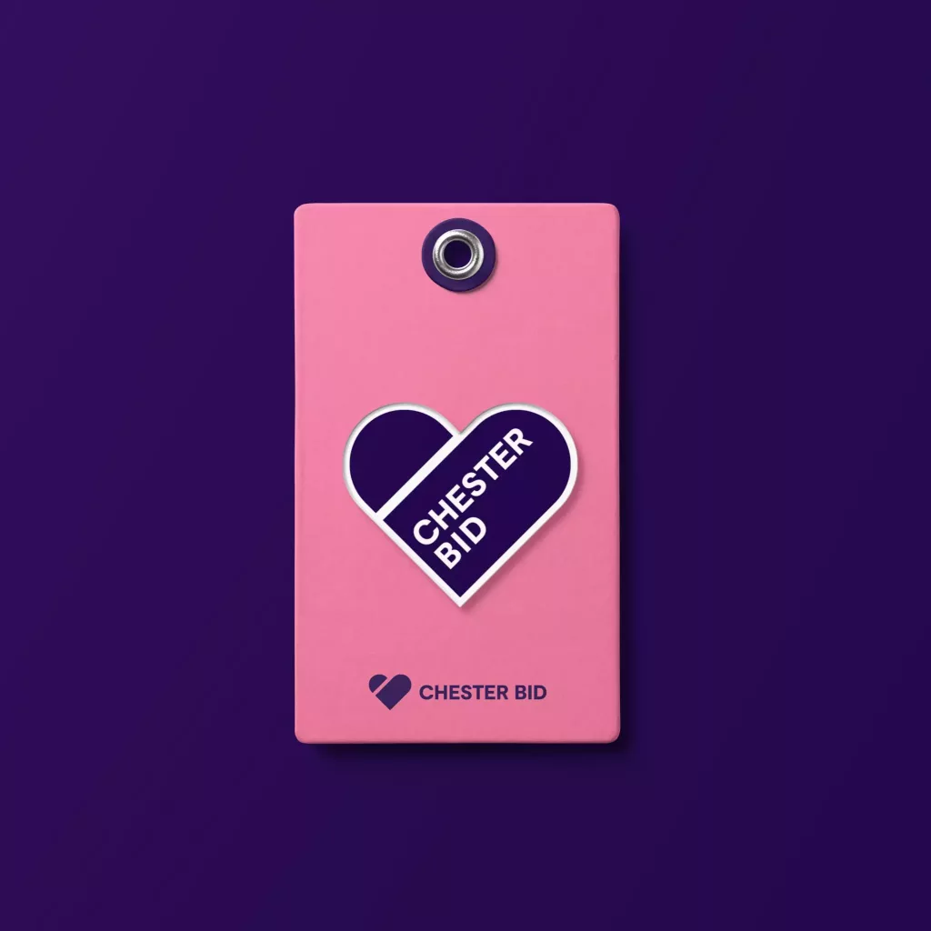 Pink luggage-style tag with a purple heart sticker reading CHESTER BID and matching logo on a purple background.
