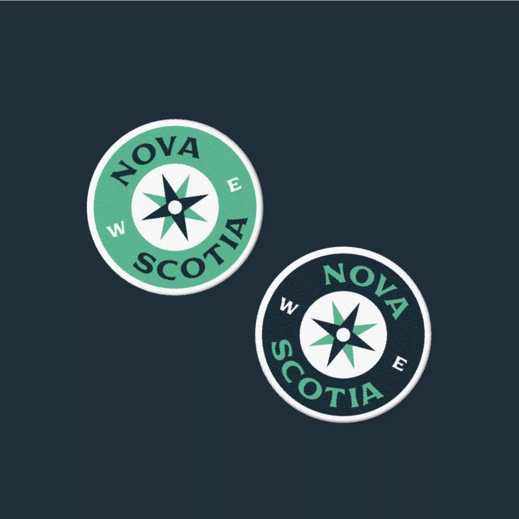 Two round embroidered Nova Scotia compass patches—one mint green, one dark navy—with a central star on a dark blue background.