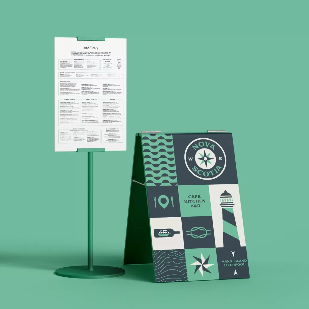 Teal cafe display with a menu stand beside an A-frame sign showing Nova Scotia compass, lighthouse and food icons.