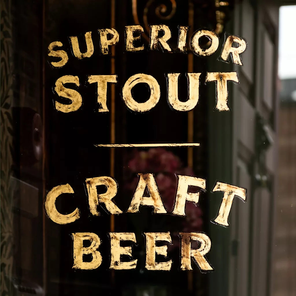 Gold brushstroke lettering on a dark shop window reading SUPERIOR STOUT and CRAFT BEER.