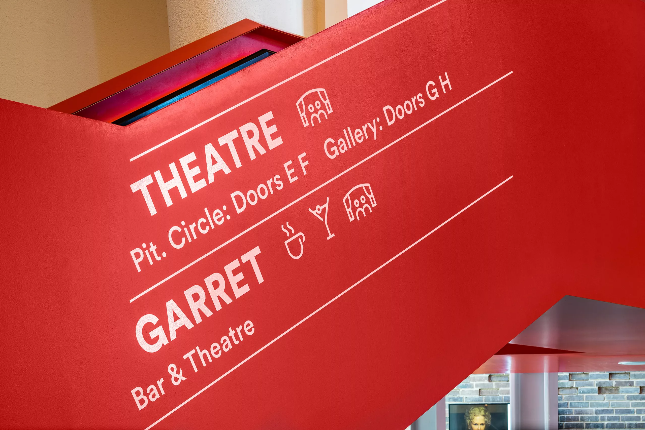 Red slanted wall with white theatre signage reading THEATRE and GARRET, door directions and icons for seating and refreshments.