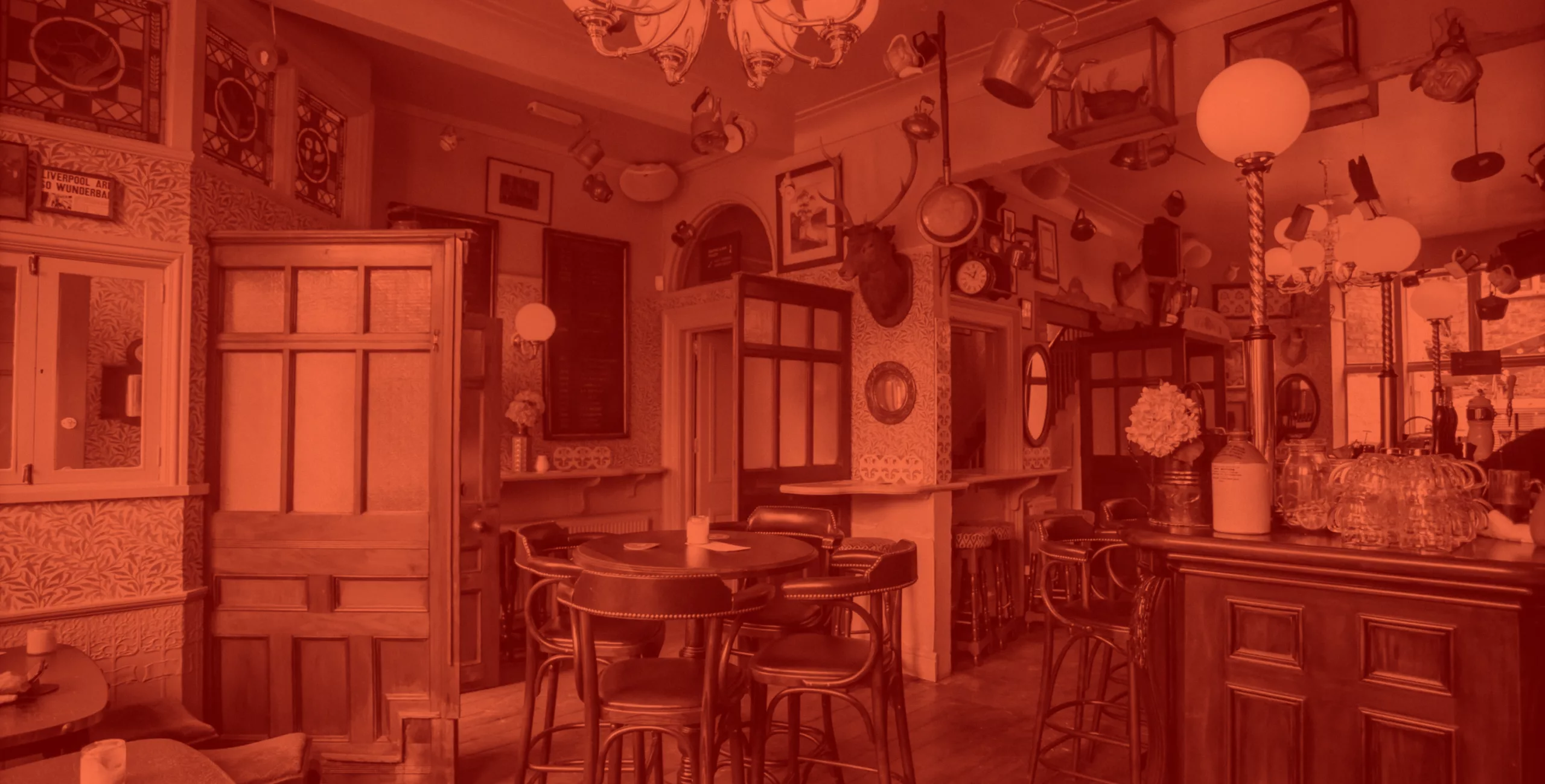 Cozy vintage pub interior with wooden bar and round high tables, leather stools, hanging lamps and mounted deer head.