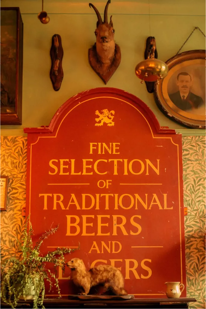 Red pub sign advertising traditional beers and lagers, topped by a horned taxidermy head.