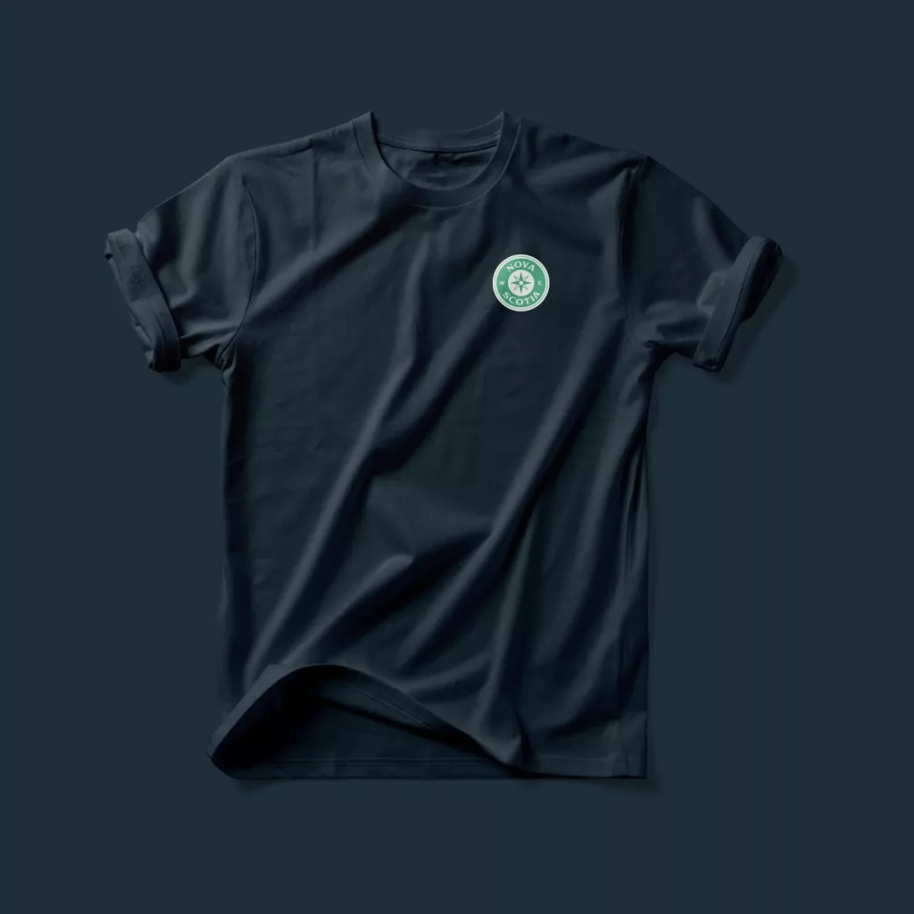 Dark navy T-shirt laid flat with rolled sleeves and a small green-and-white Nova Scotia compass logo on the left chest.