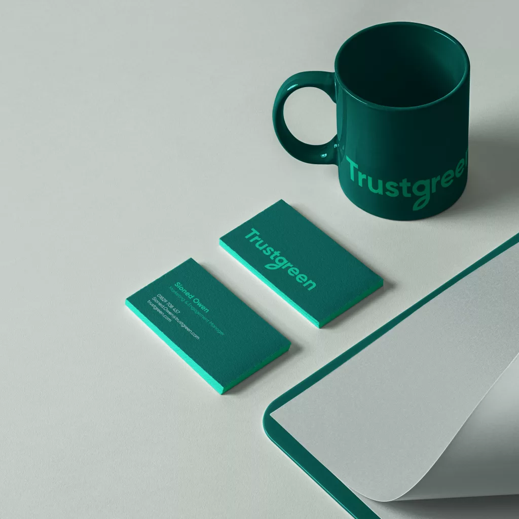 Teal mug printed Trustgreen with two matching teal business cards with neon-green edges on a pale desk