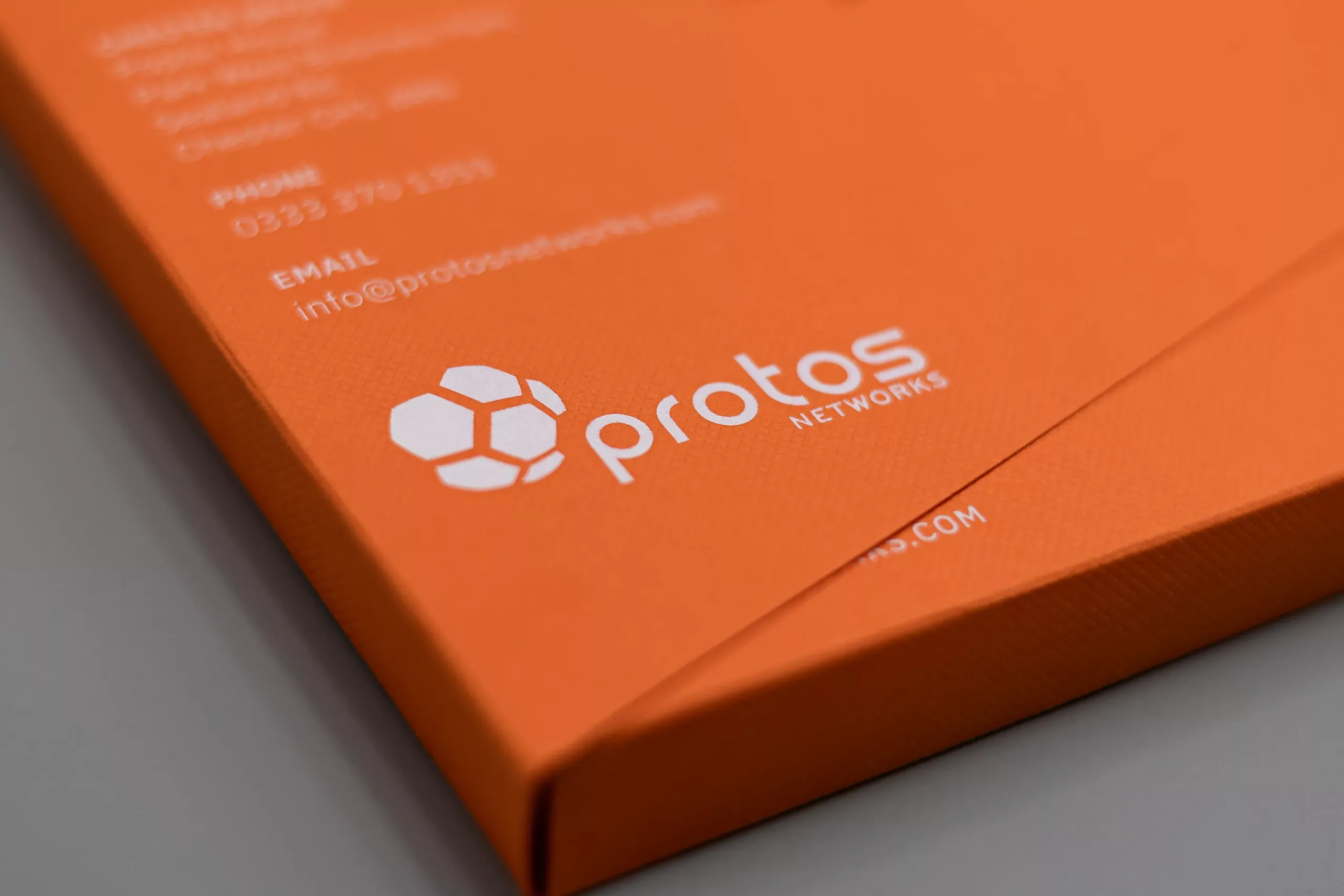 Orange packaging featuring a white protos networks logo and a hexagonal network icon