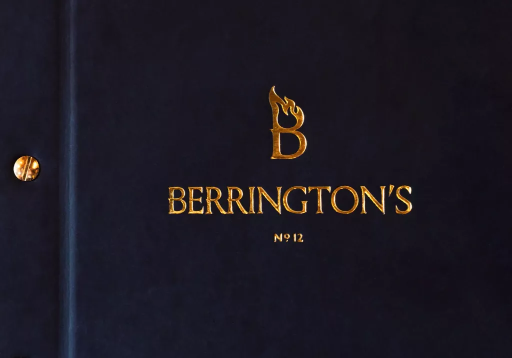 Dark blue book cover with gold embossed B flame logo, BERRINGTON'S title and No 12 beneath, brass screw at left.