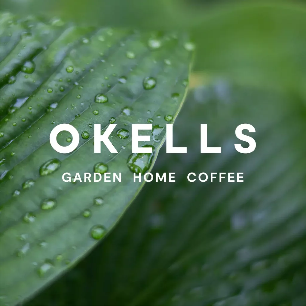 Close-up of a green leaf with water droplets, white overlaid text reading OKELLS and smaller text GARDEN HOME COFFEE