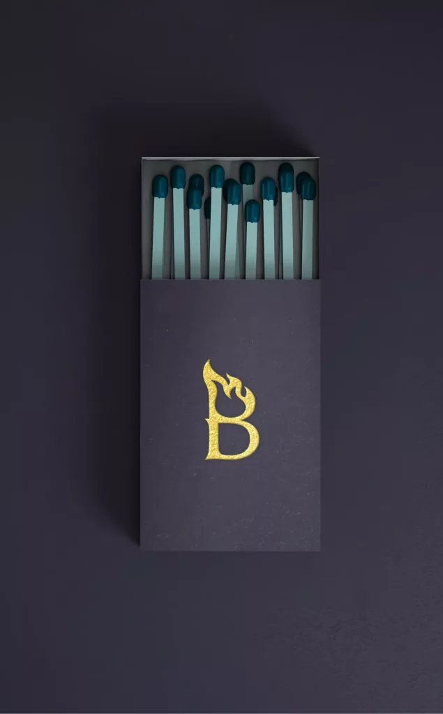 Dark purple matchbox with teal-tipped matches and a gold letter B logo incorporating a flame motif.
