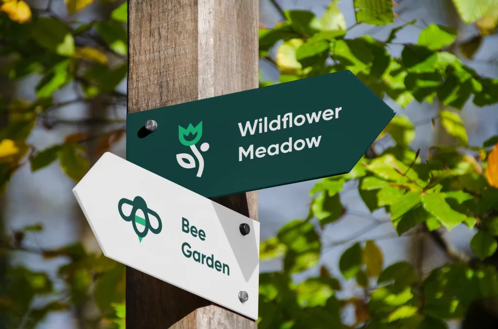 Wooden post with green arrow reading Wildflower Meadow and white arrow reading Bee Garden against a leafy background