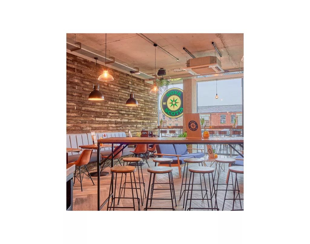 Modern café interior with wooden plank wall, pendant lights, high stools and a round Nova Scotia sign in the window.