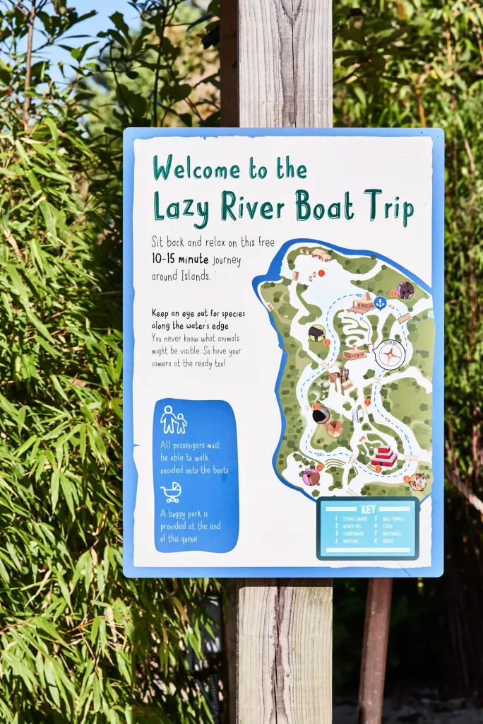 Sign reading Welcome to the Lazy River Boat Trip with illustrated island map, 10–15 minute trip info and icons, mounted on a wooden post