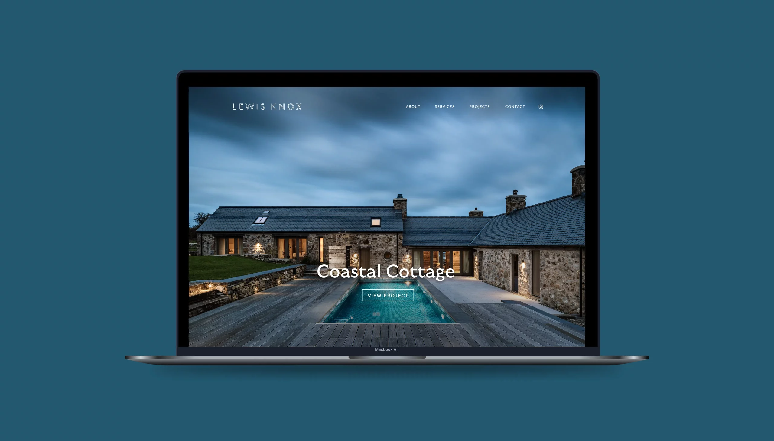 Laptop on teal background showing a website of a stone coastal cottage at dusk with pool and wooden deck.