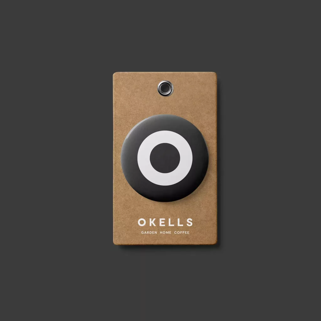 Kraft paper hang tag with metal eyelet, black circular badge with white ring and OKELLS Garden Home Coffee logo.