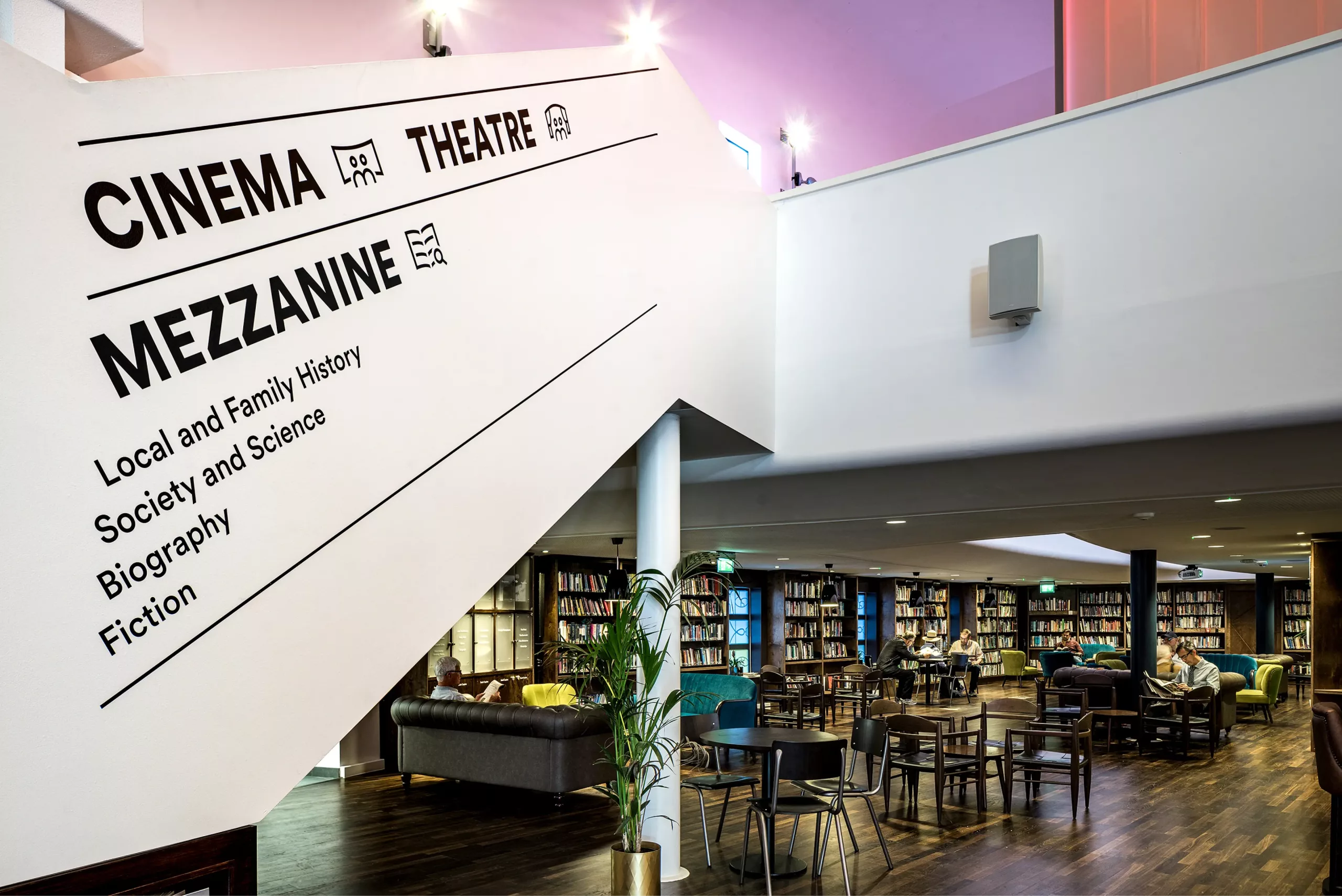 White mezzanine wall labelled CINEMA THEATRE MEZZANINE above a cosy library with bookshelves, tables and sofas