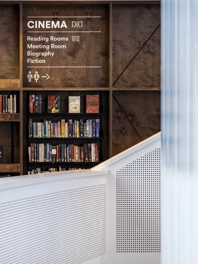 Wood-panelled library wall with white CINEMA signage above shelves of books and a white perforated counter in foreground.