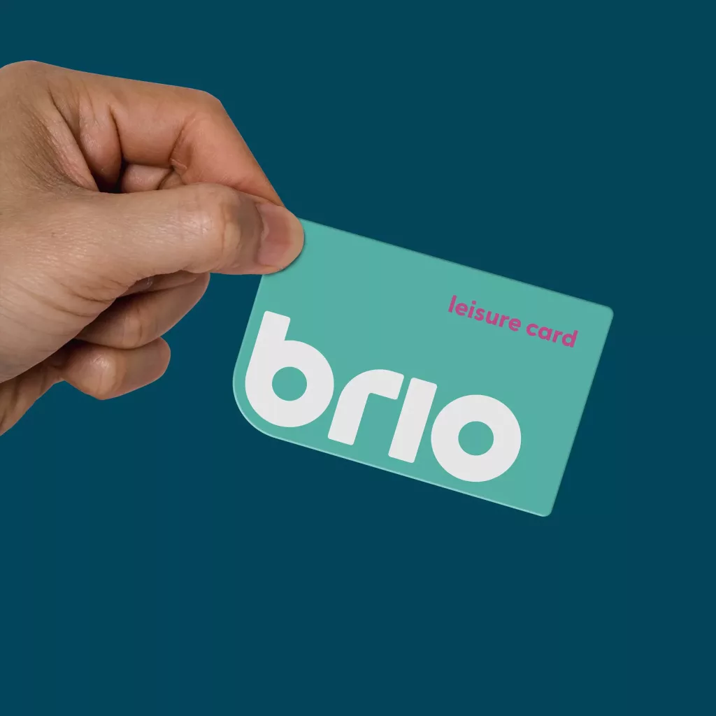 Hand holding a teal leisure card showing a large white brio logo and small pink leisure card text on a dark teal background.